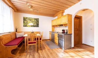 A cozy kitchen with wooden paneling and a dining area. The light falls through a window and creates an inviting atmosphere.