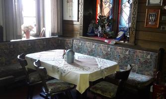 A cozy room with a round table and chairs. The walls are made of wood and the window has decorative glazing.