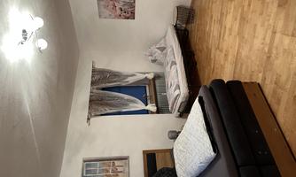 A cozy bedroom with a large bed and an additional bed. The walls are decorated with pictures, and the room has large windows with curtains.