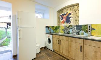 A modern kitchen with wooden cabinets and a refrigerator.  
On the wall is a colorful painting and there is a washing machine.