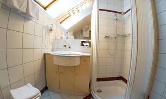 A modern bathroom with a shower and sink. The walls are tiled, and there is a window for daylight.