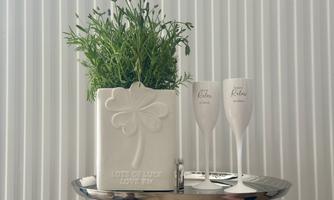 An elegant table with a white pot planted with fresh herbs. Next to it, there are two champagne glasses on a silver tray.