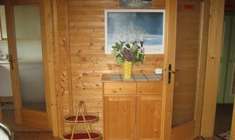 A cozy entrance area with wooden paneling. A blooming vase stands on a table and a beautiful picture hangs on the wall.
