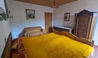 A cozy bedroom with a large bed and a yellow blanket. In the room, there is a sofa, a wardrobe, and various pictures on the wall.
