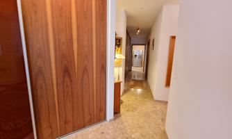 A bright hallway with a wooden wardrobe and light flooring. At the end of the hallway, more doors are visible.