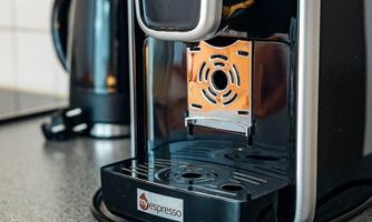 An elegant espresso machine is on a kitchen countertop. In the background, a kettle is visible.
