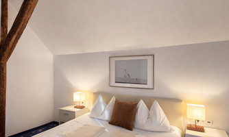 A cozy bedroom with a large bed and wooden ceiling. Two nightstands with lamps and a decorative picture on the wall.