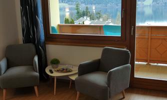 A cozy living area with two gray armchairs and a small table. Through the window, there is a view of a quiet landscape with water and trees.