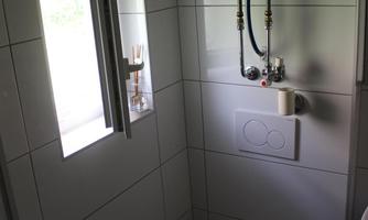 A small bathroom with bright tiles and a window. There is a toilet and a wall with water connections.