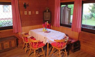 A cozy dining area in a wooden house with a table and colorful chairs. Red cushions and checked curtains give the room a rustic charm.