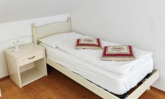 A simple bedroom with a white bed and two pillows on the mattress. Next to the bed is a nightstand with a lamp.