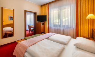 A cozy hotel room with two beds, a television, and a table. Large windows let in plenty of daylight.