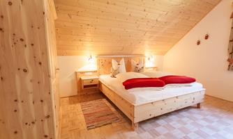 A cozy bedroom with wood paneling and a double bed. Red pillows and a carpet give the room a warm atmosphere.