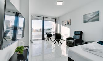 A modern room with large windows and plenty of daylight. It is equipped with a television, a desk, and comfortable chairs.