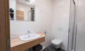 A modern bathroom with a bright shower cubicle and a sink on a wooden shelf. The walls are tiled in light colors, and there is a large mirror.