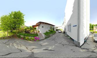 A beautiful garden with colorful flowers and a single-family house. Some cars are parked on the street, and the surroundings are green and inviting.