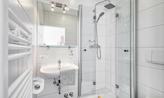 A modern bathroom with a glass shower and a sink. White tiles and a towel holder can also be seen.