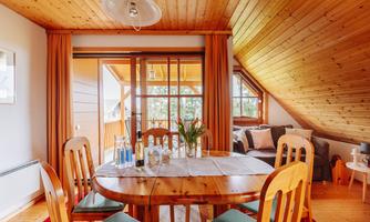 A cozy dining area with a round wooden table and chairs. Large windows provide a view of the terrace and plenty of natural light.