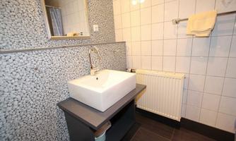 A modern bathroom with a sink on an elegant vanity. The walls are partially decorated with light tiles and pebbles.