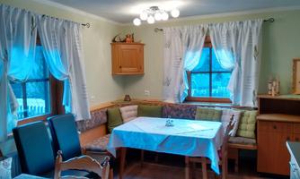 A cozy dining area with a table and a bench. The windows are covered with light curtains and the room is friendly and inviting.