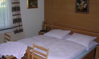 A simple bedroom with a double bed and a table. A picture hangs on the wall and there is a small area with chairs.