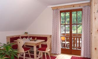A cozy dining area with a wooden table set and red chairs. Large windows offer a view of nature and the balcony.
