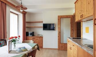A cozy kitchen with wooden shelves and a dining table. The room has bright walls and a large window.