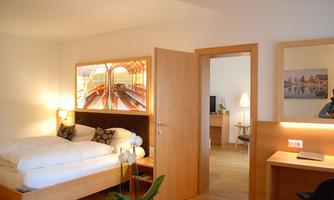 A modern bedroom with a large bed and a wooden desk. The room is bright and inviting, with a beautiful picture on the wall.