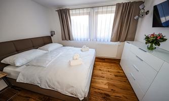A cozy bedroom with a large bed and fresh towels. There is a white wardrobe, a television, and a beautiful bouquet of flowers on the dresser.