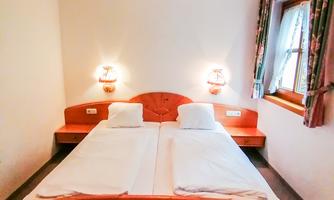 A simple bedroom with two beds, a wooden dresser, and soft lights. The room has a cozy, rustic style.