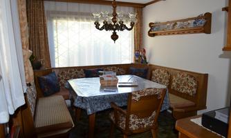 A cozy dining area with a round table and upholstered chairs. Subtle decorations and plenty of natural light through the window create an inviting atmosphere.