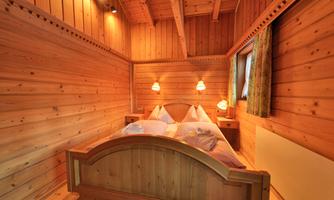 A cozy bedroom with wooden walls and a double bed. The warm lights create an inviting atmosphere.