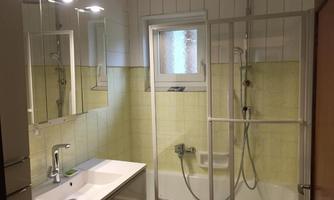A modern bathroom with a bathtub and shower. The walls are tiled in light yellow, and there are large mirrors above the sink.