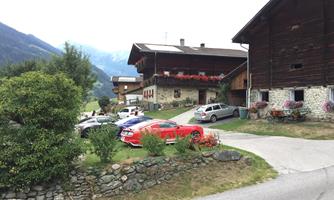 A picturesque mountain village with traditional wooden houses and blooming plants. Parked cars blend harmoniously into the rural surroundings.