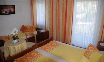 A cozy room with two beds and bright yellow bedding. A small seating area with a table and decorated with flowers, as well as a television on the wall.