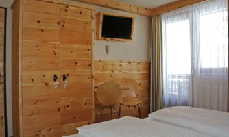 A bright bedroom with wooden furniture. There is a wardrobe, a television, and two chairs.