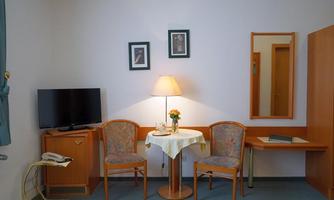 A cozy room with a round table and two chairs. Pictures hang on the wall, and a television stands on a wooden cabinet.