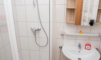 A modern bathroom with a shower and a sink. The walls are tiled and there is a wooden floor.