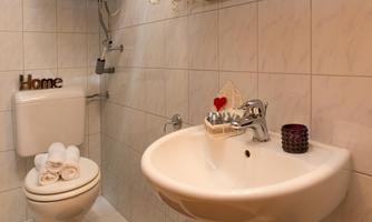 A modern bathroom with white tiles and a sink. There are towels, a toilet, and decorative elements.