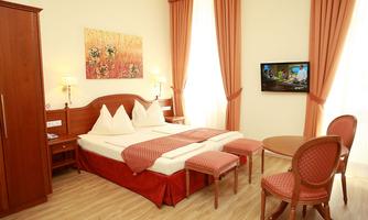 A cozy hotel room with a double bed, wooden furniture, and a flat-screen TV. Partially light curtains and a table with chairs complete the ambiance.