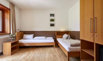 A bright room with two wooden single beds. The walls are painted in soft colors and there are some pictures on the wall.