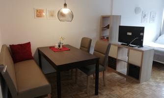 A cozy dining area with a table, chairs, and a bench. In the background, there is a television and a shelf.