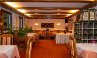 A cozy restaurant with wooden ceilings and warm lighting. The tables are neatly set and plants create a pleasant atmosphere.