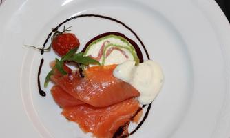 An elegant dish with smoked salmon, a cream sauce, and a decorative tomato element. In addition, fresh vegetables are arranged on the plate.