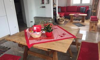 A cozy dining area with a wooden table and red cushions. On the table, there is a fruit bowl and a flower in a pot.