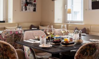 A stylish restaurant with a table set with drinks and dishes. The cozy chairs have a floral design, and the space offers an inviting atmosphere.