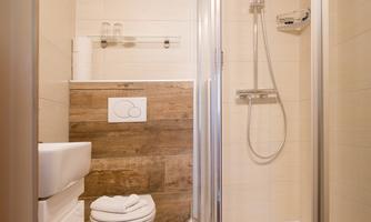 A modern bathroom with shower and toilet. The walls are tiled in light colors, the floor has a wood look.