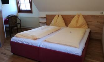 A cozy bedroom with a large double bed and two pillows. There is also a chair and a television on the wall.
