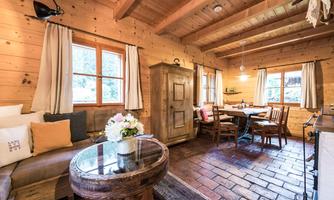 A cozy room with wooden paneling, a round table, and a sofa corner. Large windows let in plenty of light, and the decor radiates warmth.