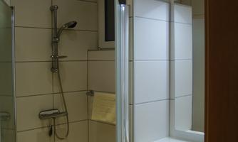 A modern bathroom with a shower cabin and a large mirror. The walls are brightly tiled and there is pleasant lighting.